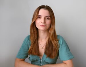Marta Rivera, autora de 'La Aventura de Lou', sonríe mientras sostiene su libro, rodeada de ilustraciones coloridas y un entorno natural inspirador.